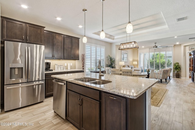 kitchen featuring a tray ceiling, stainless steel appliances, light stone countertops, dark brown cabinetry, and sink