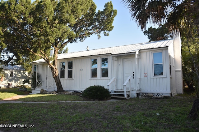 view of front of house featuring board and batten siding, entry steps, metal roof, and a front yard