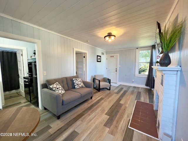 living area with a brick fireplace, crown molding, baseboards, and wood finished floors