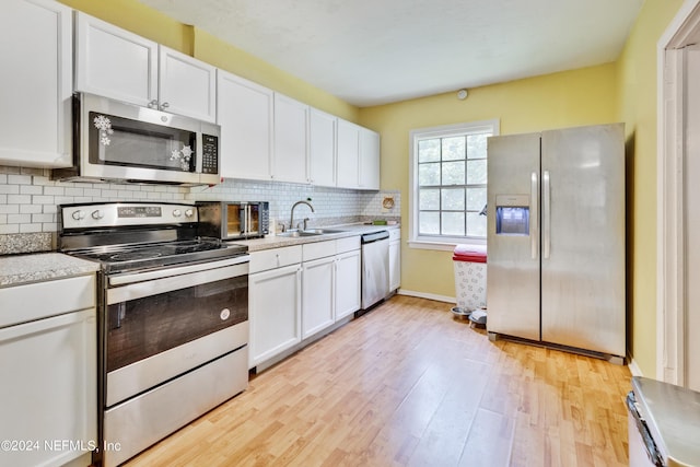 kitchen with appliances with stainless steel finishes, light hardwood / wood-style floors, white cabinetry, and sink