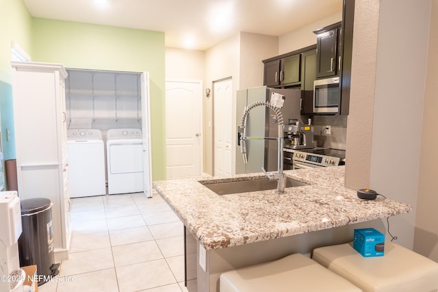 kitchen featuring washing machine and dryer, a kitchen bar, light stone counters, appliances with stainless steel finishes, and light tile patterned floors