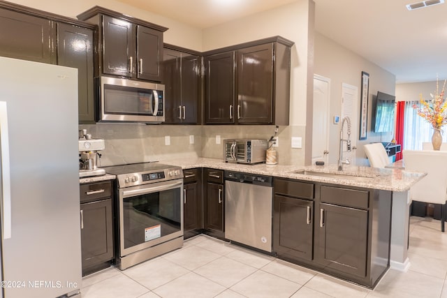 kitchen featuring light tile patterned flooring, sink, light stone counters, appliances with stainless steel finishes, and backsplash