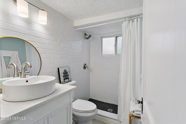 bathroom with a textured ceiling, toilet, vanity, tile walls, and curtained shower