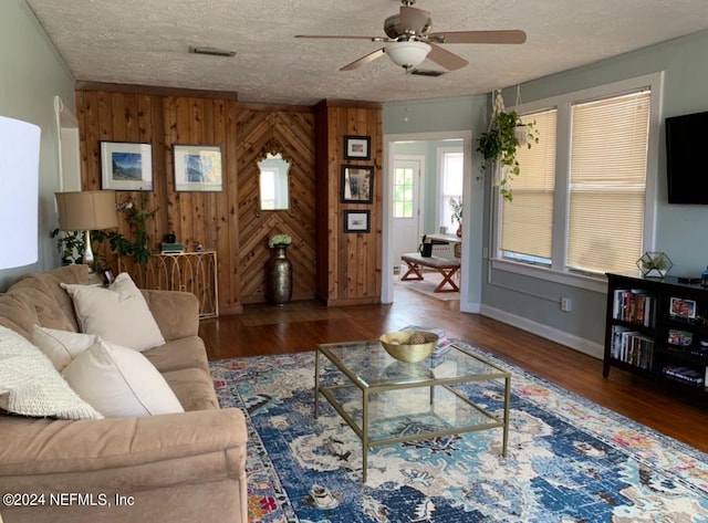 living room featuring ceiling fan, a textured ceiling, wooden walls, and wood-type flooring