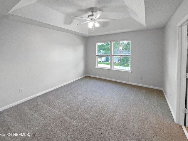 carpeted spare room featuring a textured ceiling, ceiling fan, and a tray ceiling