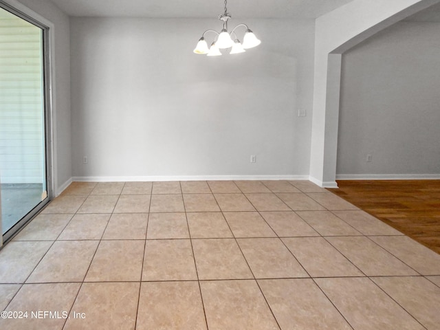 tiled spare room with a notable chandelier