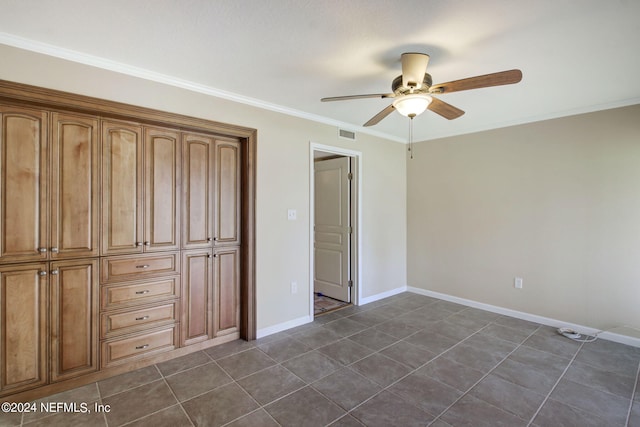 unfurnished bedroom with ceiling fan, dark tile patterned flooring, ornamental molding, and a closet