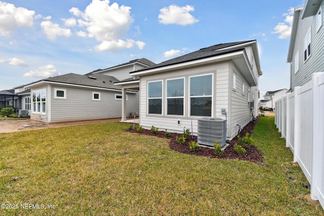 rear view of house with central AC unit and a lawn