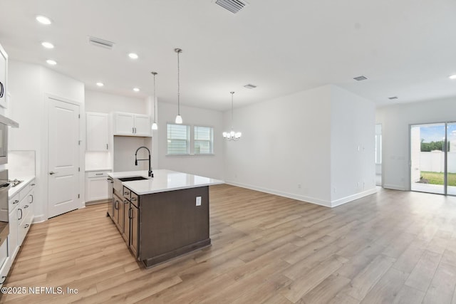 kitchen with sink, light wood-type flooring, white cabinetry, an island with sink, and an inviting chandelier