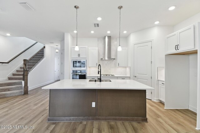 kitchen featuring white cabinetry, wall chimney range hood, wall oven, and hanging light fixtures