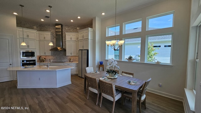 kitchen featuring stainless steel appliances, brick wall, wall chimney range hood, and hanging light fixtures