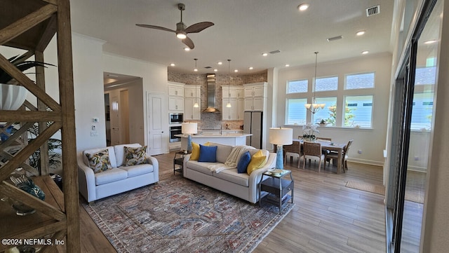 living room with ceiling fan with notable chandelier, ornamental molding, and light hardwood / wood-style flooring