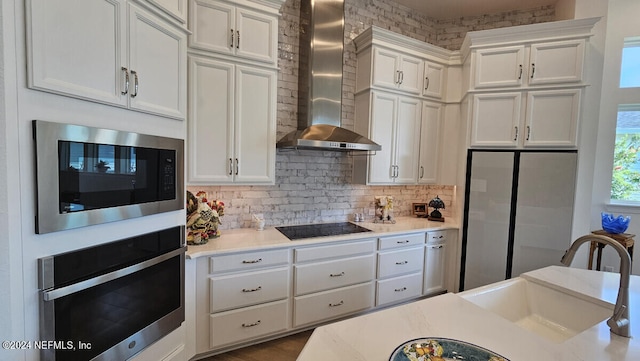 kitchen featuring sink, white cabinetry, wall chimney exhaust hood, decorative backsplash, and black appliances