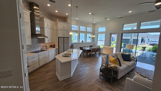 kitchen with dark wood-type flooring, pendant lighting, a center island, wall chimney range hood, and white cabinetry