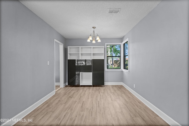 interior space with light wood-type flooring, a notable chandelier, and a textured ceiling