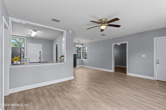 unfurnished living room featuring sink, ceiling fan with notable chandelier, a textured ceiling, and light wood-type flooring