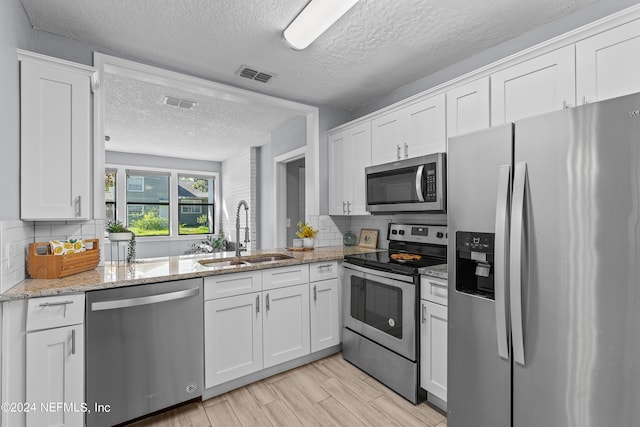 kitchen with sink, appliances with stainless steel finishes, backsplash, light stone counters, and white cabinets