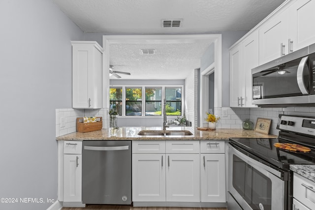 kitchen with appliances with stainless steel finishes, backsplash, light stone counters, white cabinets, and a textured ceiling