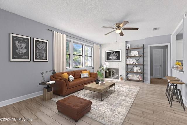 living room featuring ceiling fan, a brick fireplace, and a textured ceiling