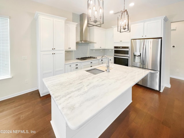 kitchen with appliances with stainless steel finishes, decorative light fixtures, a center island with sink, and wall chimney exhaust hood