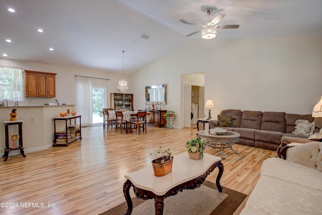 living room featuring washer / clothes dryer, high vaulted ceiling, ceiling fan with notable chandelier, and light hardwood / wood-style floors