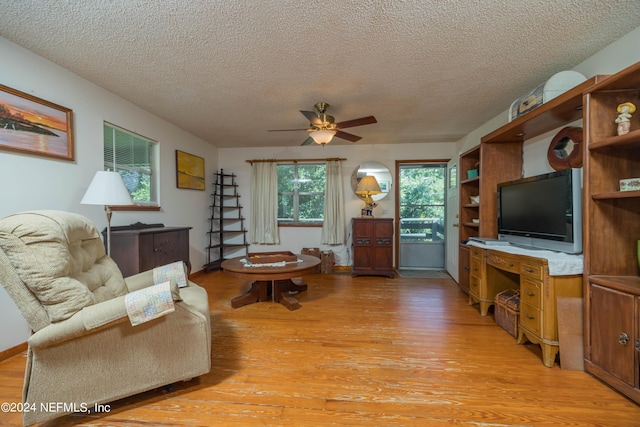 living room with ceiling fan, a textured ceiling, and light wood-type flooring