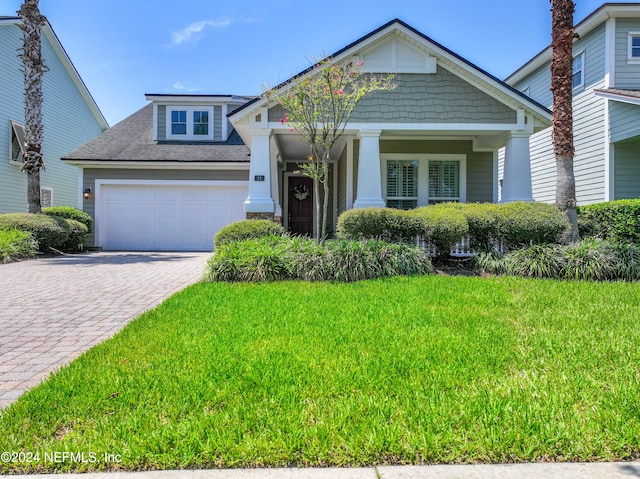 craftsman inspired home featuring a garage, a front lawn, decorative driveway, and a shingled roof