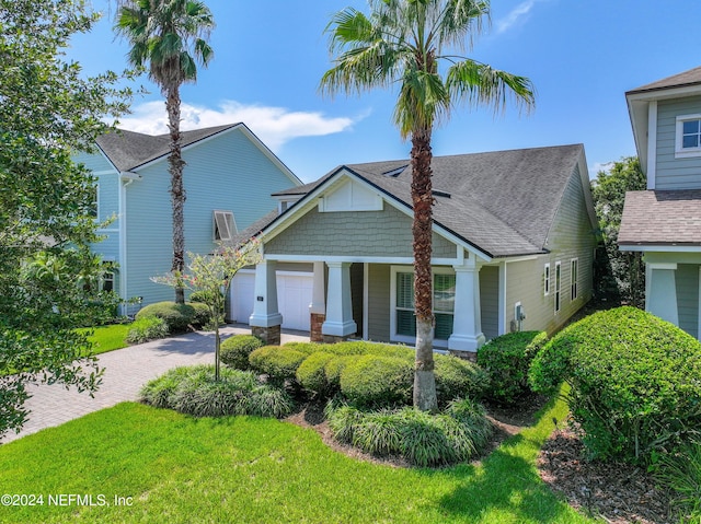 craftsman inspired home with a garage, roof with shingles, a front lawn, and decorative driveway