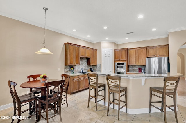 kitchen with arched walkways, stainless steel appliances, hanging light fixtures, brown cabinetry, and a kitchen island