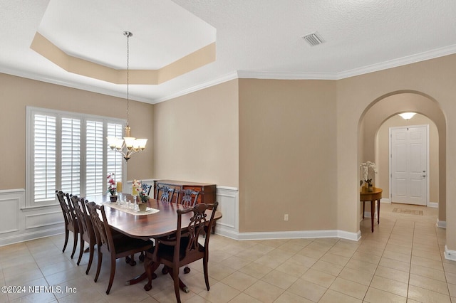 dining room with a tray ceiling, arched walkways, a wainscoted wall, light tile patterned floors, and visible vents