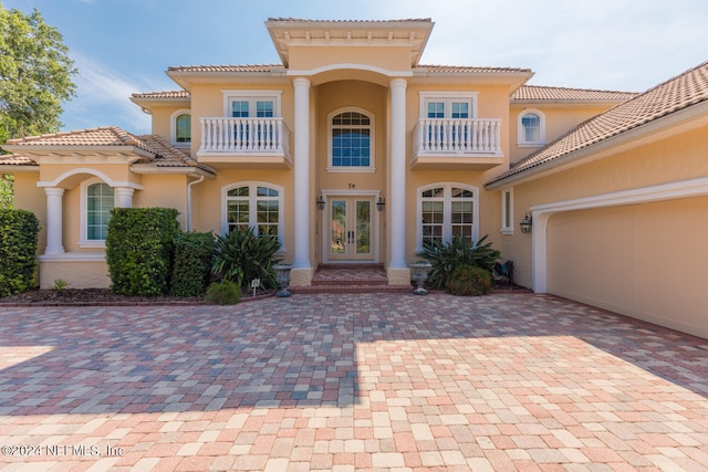 mediterranean / spanish home with french doors, stucco siding, a balcony, a garage, and a tiled roof