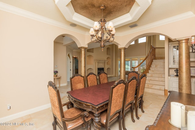 dining room with arched walkways, a chandelier, baseboards, a tray ceiling, and ornate columns