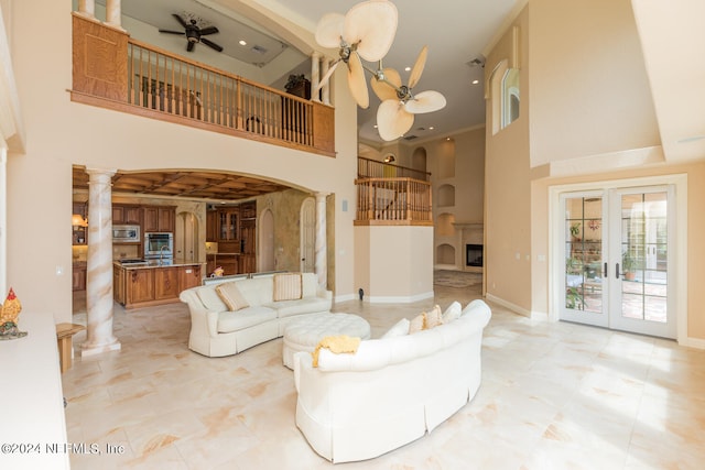 living room featuring ceiling fan, arched walkways, a high ceiling, baseboards, and decorative columns