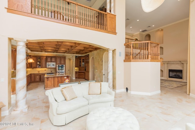 living room featuring arched walkways, a high ceiling, ornamental molding, coffered ceiling, and ornate columns