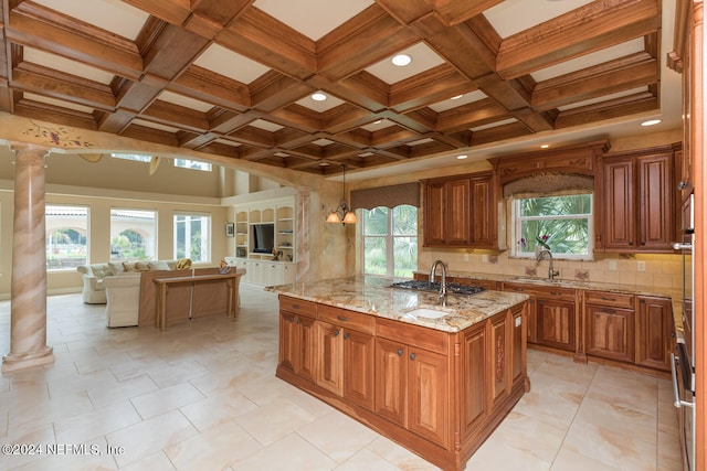 kitchen featuring brown cabinets, decorative columns, a center island with sink, backsplash, and open floor plan