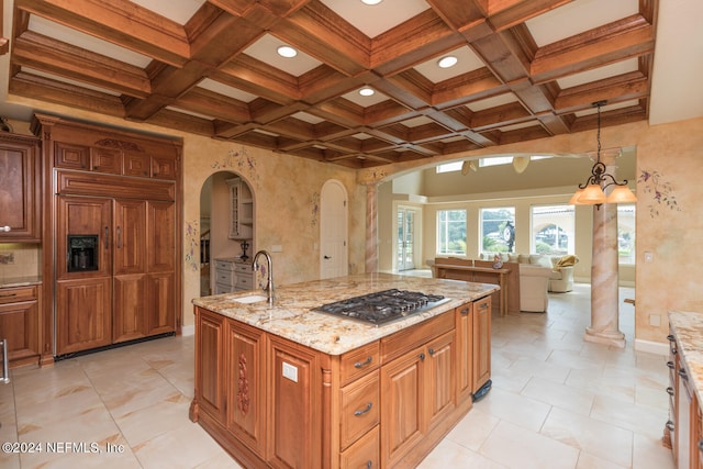 kitchen with arched walkways, coffered ceiling, light stone countertops, stainless steel gas cooktop, and a sink