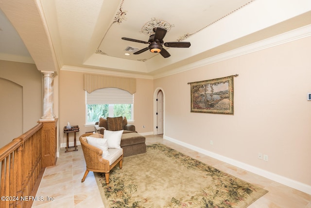 sitting room with arched walkways, ceiling fan, ornamental molding, a tray ceiling, and decorative columns