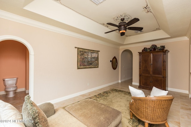 living room featuring arched walkways, ceiling fan, ornamental molding, a tray ceiling, and light tile patterned flooring