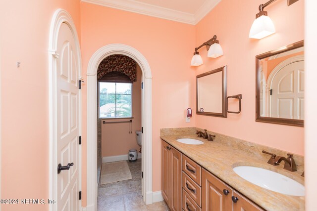 bathroom featuring double vanity, ornamental molding, toilet, and a sink