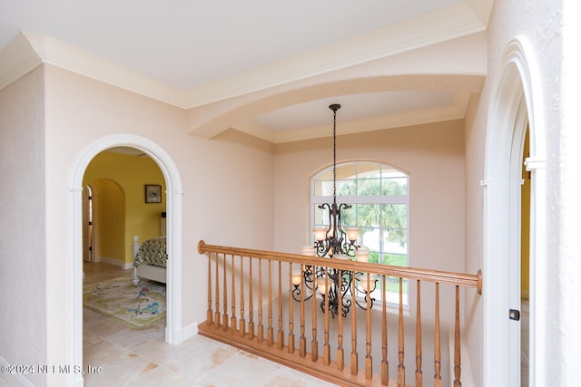 hallway featuring light tile patterned floors, baseboards, arched walkways, ornamental molding, and a chandelier