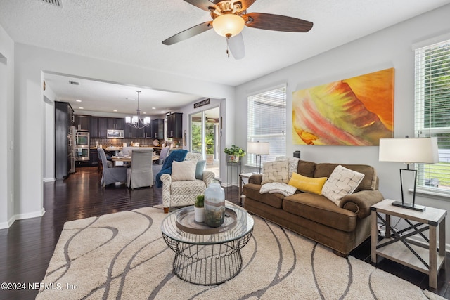 living room featuring a textured ceiling, dark wood-type flooring, a healthy amount of sunlight, and ceiling fan with notable chandelier