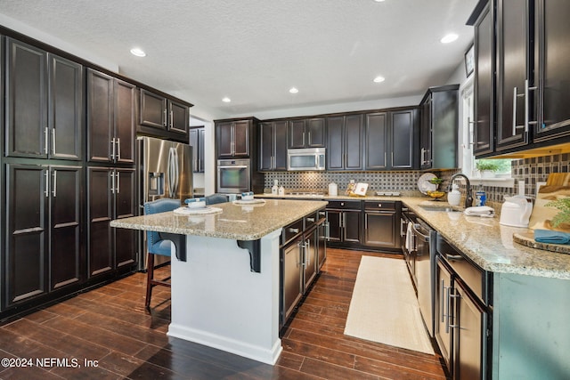 kitchen with sink, a breakfast bar area, a kitchen island, stainless steel appliances, and light stone countertops