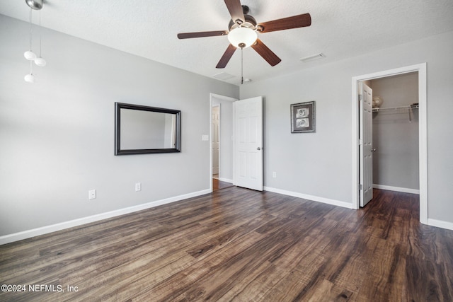 unfurnished bedroom featuring a walk in closet, a textured ceiling, dark hardwood / wood-style floors, a closet, and ceiling fan