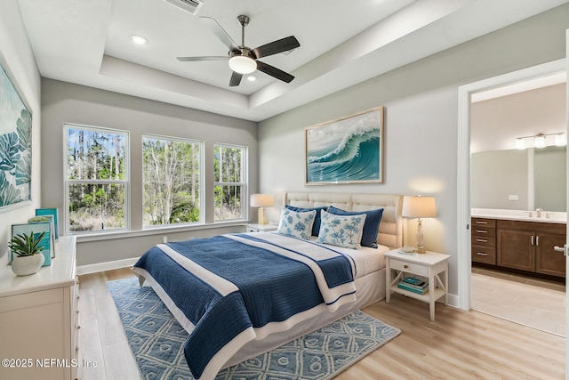 bedroom with recessed lighting, ensuite bath, light wood-type flooring, and a tray ceiling