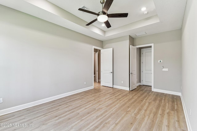 unfurnished bedroom with visible vents, baseboards, ceiling fan, a raised ceiling, and light wood-type flooring