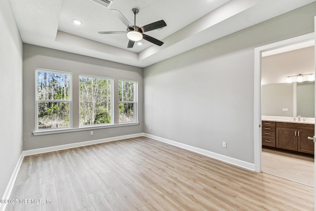 spare room with a raised ceiling, light wood-style flooring, baseboards, and ceiling fan