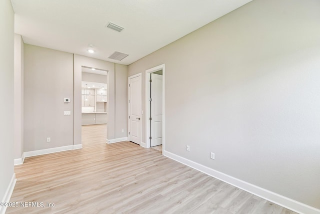 spare room featuring light wood-style floors, visible vents, and baseboards