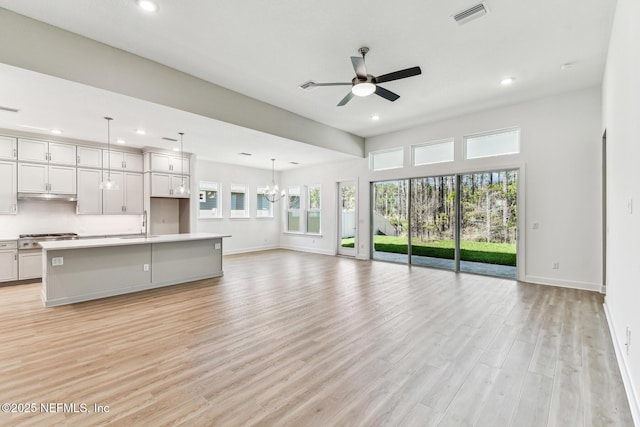 unfurnished living room featuring light wood finished floors, visible vents, ceiling fan with notable chandelier, and recessed lighting