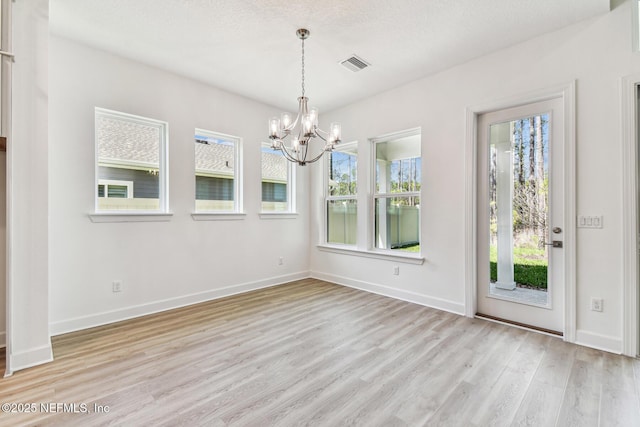 unfurnished dining area featuring visible vents, a notable chandelier, a textured ceiling, light wood finished floors, and baseboards