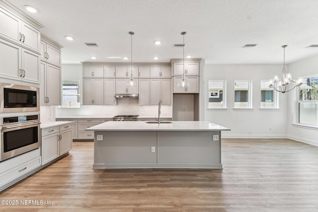 kitchen with visible vents, built in microwave, stainless steel oven, gray cabinets, and a sink